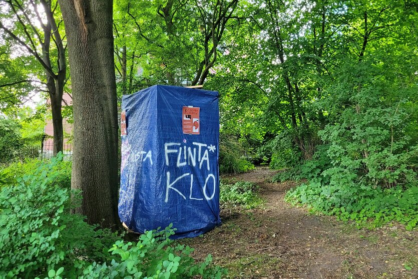 Eine Kabine aus blauer Plane mit der Aufschrift "Flinta* Klo".
