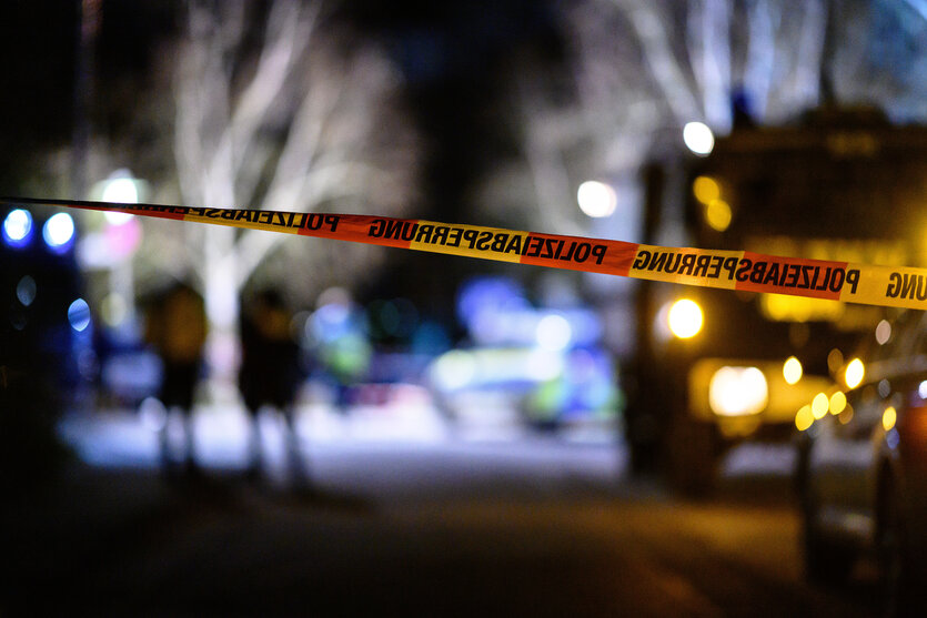 Ein Flatterband der Polizei ist vor Einsatzfahrzeugen am Tatort zu sehen, hier erschosse die Polizei einen Mann