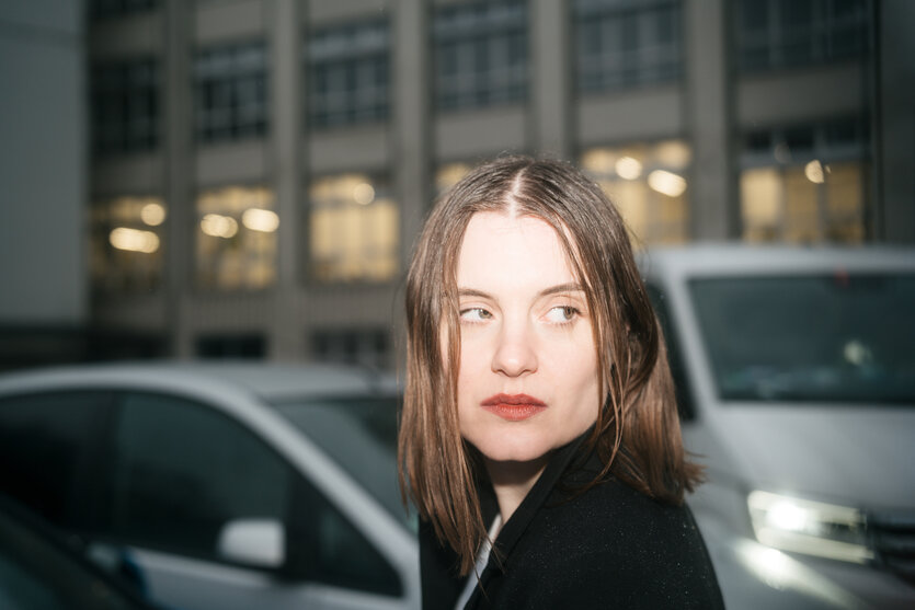 Sophia Kennedy blickt sich um, im Hintergrund Autolichter und erleuchtete Gebäude, es ist dunkel.
