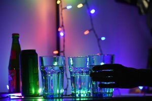 In einem Club stehen Getränke auf einer Theke. Eine Hand greift nach einem vollen Glas