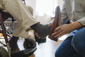 Eine Person zieht einer anderen Person, die im Rollstuhl sitzt, Schuhe an