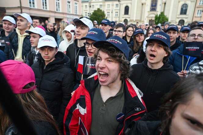 Junge Männer mit Basecaps auf dem Kopf stehen auf einer Kundgebung und schreien rum