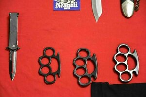 Auf einem roten Untergrund liegen verschiedene Waffen, wie Messer und Schlagringe