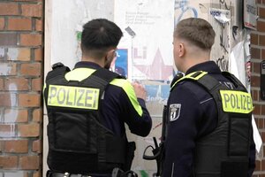 Zwei Polizisten vor einer Hauswand mit Plakaten. Das Foto von Yoran Lischinky ist im Anriss erkennbar.