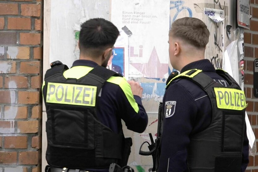 Zwei Polizisten vor einer Hauswand mit Plakaten. Das Foto von Yoran Lischinky ist im Anriss erkennbar.
