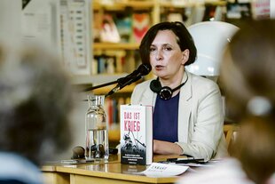 Klementyna Suchanow sitzt am Rednerpult, vor ihr ihr Buch "Das ist Krieg"