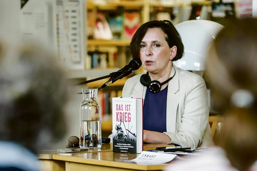 Klementyna Suchanow sitzt am Rednerpult, vor ihr ihr Buch "Das ist Krieg"