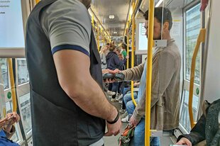 Eine Szene aus einer Tram während einer Ticketkontrolle, der Kontrolleur hält sein Lesegerät an das digitale Ticket eines Mannes