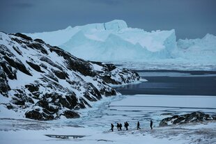 Eine Gruppe Touristen wandert in der Nähe des grönländischen Ortes Ilulissat vor der Kulisse riesiger Eisberge entlang. Die Eisberge sind vom nahegelegenen Gletscher Sermeq Kujalleq gekalbt