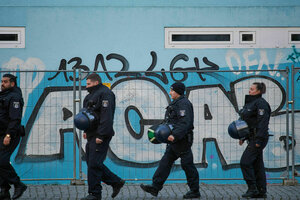 Polizisten gehen an einer Hauswand entlang, auf die eine Graffiti gemalt ist