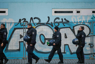 Polizisten gehen an einer Hauswand entlang, auf die eine Graffiti gemalt ist