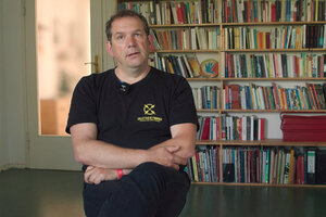 Lars Hirsekorn sitzt in T-Shirt in einem Zimmer vor einer Bücherwand