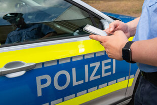 Ein Polizist nutzt neben einem Polizeiauto in ein Smartphone