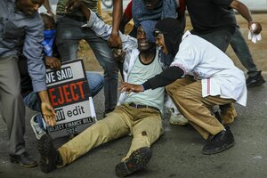 Ein Mann sitzt auf dem Boden, sein Bein ist angeschossen. Weiter Menschen beugen sich zu ihm hinunter