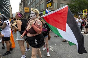 Eine Person in einem Netz-Oberteil und mit weiß geschminktem Gesicht trägt eine Palästina-Fahne