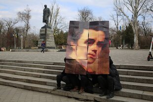 Eine Statue von Taras Schwetschenkound Menschen, die sich sein Konterfei vor ihre Gesichter halten