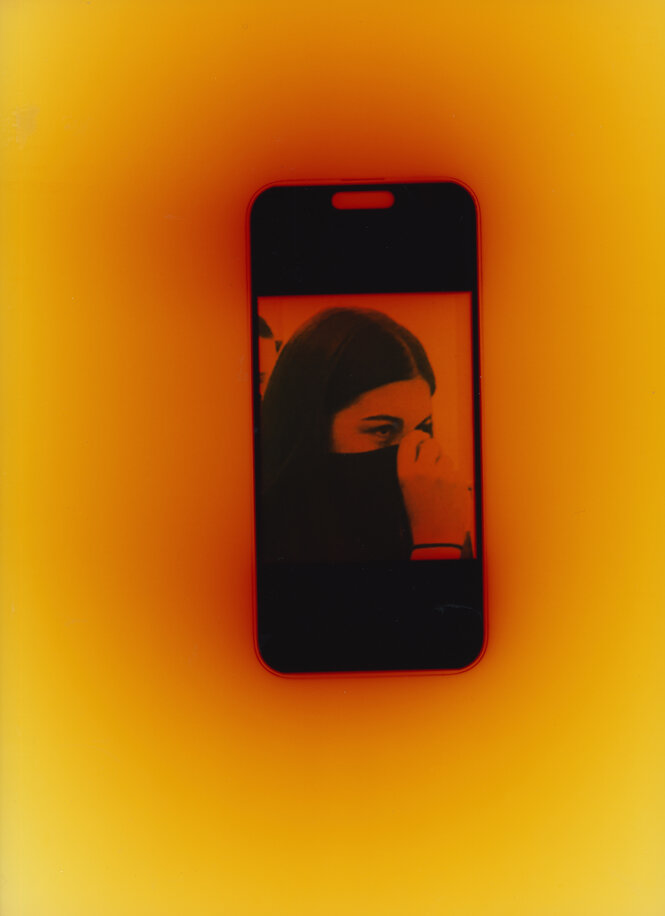 Auf einem gelb-roten Grund ist ein schwarz-weißes Handyfoto von einer Person, die sich das Gesicht mit der Hand verdeckt