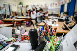 Stifte, Hefte, eine Musikbox liegen auf einem Tisch im Klassenzimmer, die Schüler sind undeutlich zu sehen