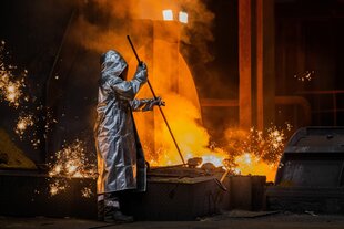 Ein Stahlarbeiter in Schutzkleidung macht einen Abstich von geschmolzenem Stahl