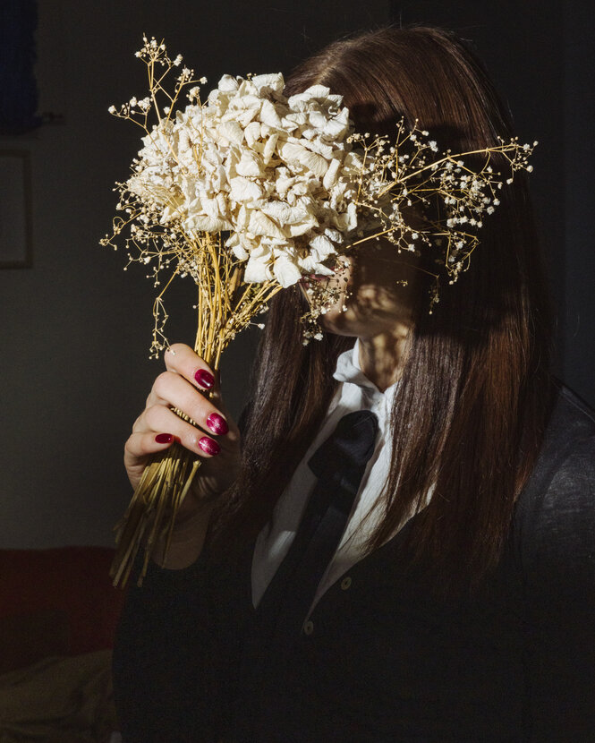Eine Person versteckt ihr Gesicht hinter Blumen.