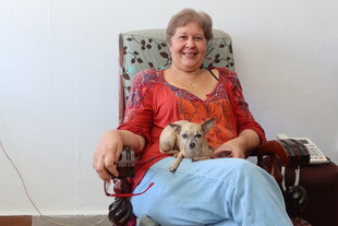 Porträt von Alina Bárbara López sitzt in einem Sessel, den Hund auf dem Beinen und lächelt