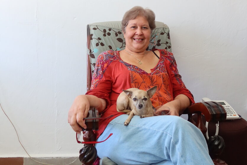Porträt von Alina Bárbara López sitzt in einem Sessel, den Hund auf dem Beinen und lächelt