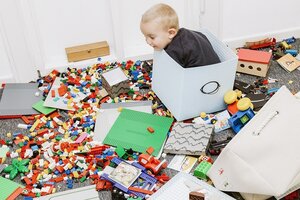 Ein Klindkind sitzt zwischen verstreuten Legosteinen in einer Spielzeugkiste