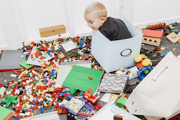 Ein Klindkind sitzt zwischen verstreuten Legosteinen in einer Spielzeugkiste