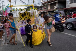 Ein Mädchen trägt ein gelbes Rüschenkleid und ist mit seiner Familie bei einer Prozession in den Straßen von Manila