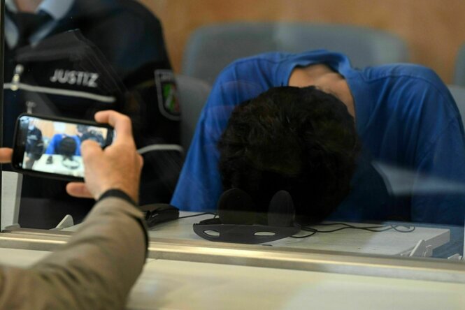 Eine Person hat ihren Kopf auf einen Tisch gelegt, eine weitere Person fotografiert diese Szene mit einem Handy