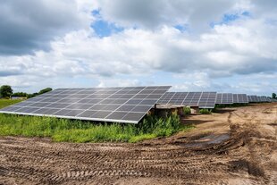 Eine Photovoltaikanlage auf einem Feld, auf dem Boden davor sieht man Spuren von Autoreifen
