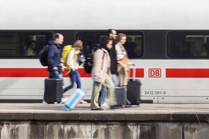 Menschen mit KOffern gehen auf einem Bahnsteig an einem ICE entlang. Sie sind in Bewegungsunschärfe abgebildet