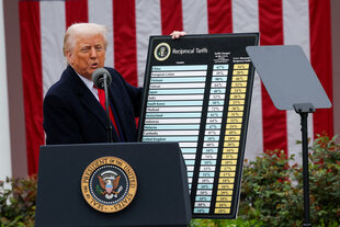 Donald Trump präsentiert auf einer Bühne eine Tabelle