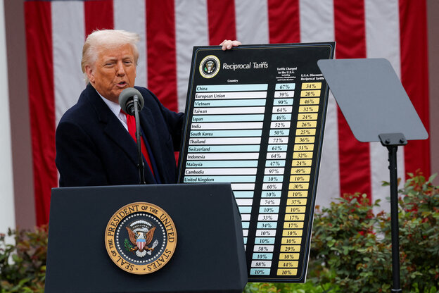 Donald Trump präsentiert auf einer Bühne eine Tabelle