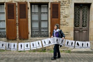 Eine Person hält ein Banner hoch, auf dem die Silhouetten von Kindern zu sehen sind, darunter steht jeweils 