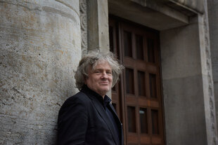 Portrait von Carl Hegemann, der vor dem Gebäude der Volksbühne steht