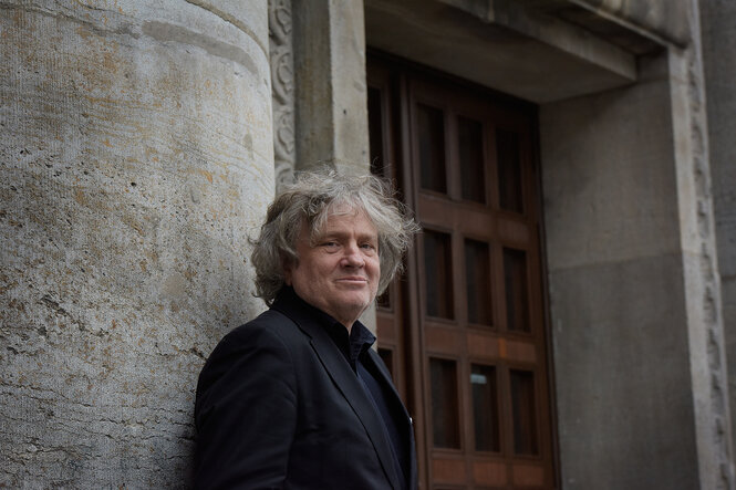 Portrait von Carl Hegemann, der vor dem Gebäude der Volksbühne steht