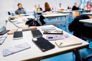 Handys liegen auf einem Tisch in einem Klassenraum.