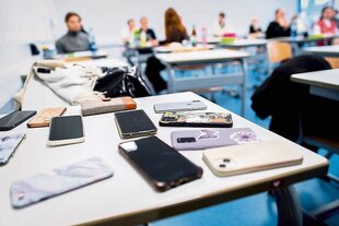 Handys liegen auf einem Tisch in einem Klassenraum.