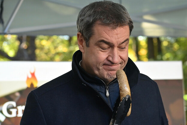 Markus Soeder haelt eine Bratwurst vor sein Gesicht