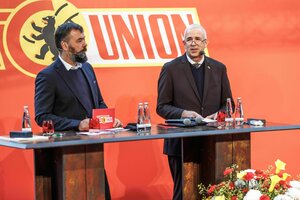Zwei Männer stehen hinter einem Tisch, im Hintergrund das Logo von Union Berlin