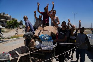 Palästinenser winken in die Kamera, während sie Kisten und Taschen mit Lebensmitteln und humanitären Hilfspaketen tragen