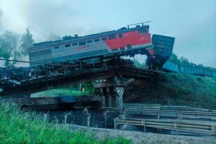 Eine zerstörte Brücke mit aufsteigendem Rauch, darauf ein Teil eines Zugs.