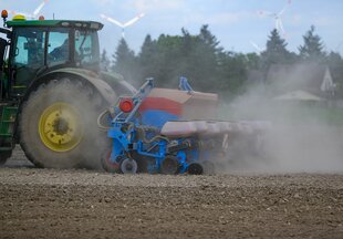 Ein Traktor zieht einen Pflug über ein sehr trockenes Feld, es staubt