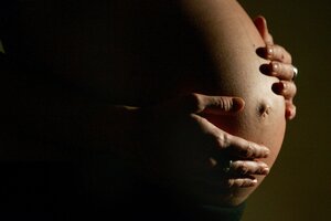 Eine hochschwangere Frau fasst sich mit beiden Händen an ihren Bauch.