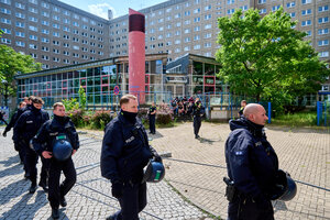 Vor einem besetzten gläsernen Gebäude sitzen menschen auf einer Treppe, davor sind Polizisten zu sehen