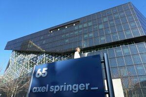 EIn Gebäude mit Glasfront, davor ein Schild mit dem Logo von Axel Springer