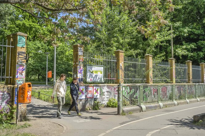 Mauer mit Zaunkrone, Menschen gehen durch ein Tor