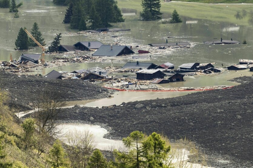 Die Dächer der Häuser des zerstörten Dorfes Blatten ragen aus Schlammwasser und Schutt