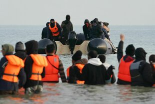 Eine Gruppe von Menschen wartet am Strand von Gravelines, um über den Ärmelkanal nach Großbritannien zu gelangen.